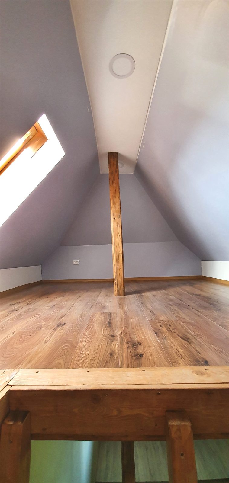 Ausgebautes Dachzimmer mit Eichenboden und sichtbarem Balken
